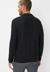 Polo a maniche lunghe nera in tessuto testurizzato, con colletto e polsini a costine. Presenta un piccolo etichetta all'orlo. Vestibilità sartoriale.