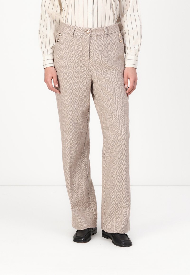 Pantalon en beige clair à motif chevrons, avec taille haute, passants pour ceinture et deux boutons décoratifs sur les poches.