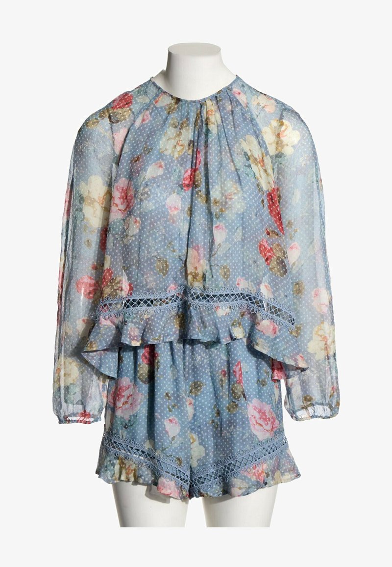 Blouse bleue transparente à motif floral avec manches longues et short assorti, les deux avec des volants et une bordure en dentelle sur un mannequin blanc.