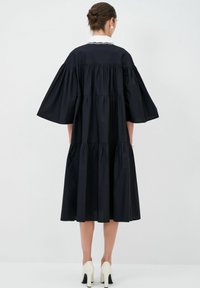 Abito nero a strati con maniche larghe, dotato di un collo bianco e bordi testurizzati, completato da una silhouette fluida e al ginocchio.
