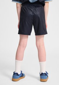 Marina sportshorts med ett strukturerat mönster, elastisk midja och en avslappnad passform, kombinerat med blå skor och vita ankelsockor.