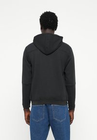 Svart hettegenser med en glatt tekstur, med kengurulomme og ribbestrikkede mansjetter, parret med lyseblå denimjeans.