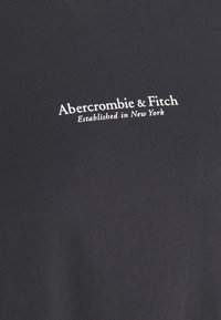 Mørkegrå bomulds-t-shirt med hvid broderet tekst, "Abercrombie & Fitch Etableret i New York," centreret på brystet.