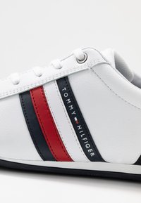 Vita sneakers med marinblå och röda ränder, med "Tommy Hilfiger"-logga på sidan och vita snören.