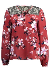 Blommig blus med rostfärgad bakgrund, spetsdetaljer, långa ärmar och en knytning vid halsen. Har rosa och vita blommor samt gröna blad.