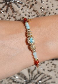 Bracelet en or orné de perles turquoises, bleu clair et rouges, avec des détails complexes, y compris des pierres précieuses claires et des accents décoratifs.