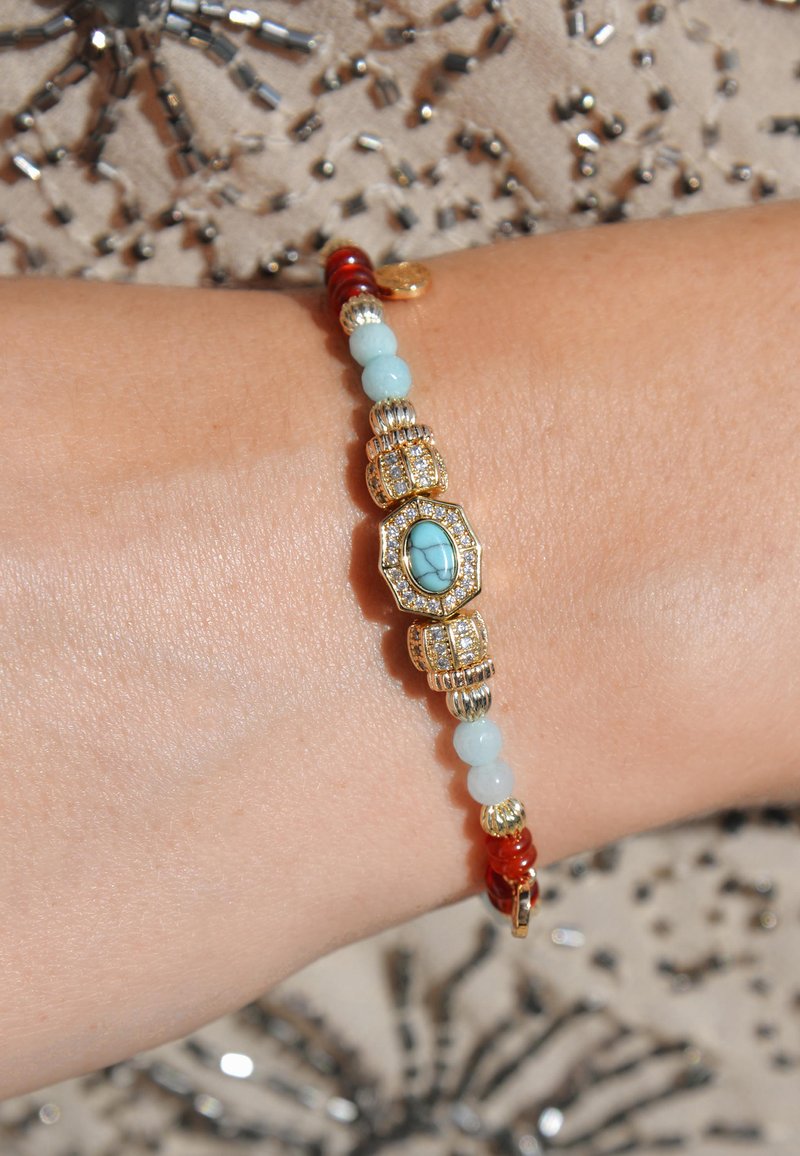 Bracelet en or orné de perles turquoises, bleu clair et rouges, avec des détails complexes, y compris des pierres précieuses claires et des accents décoratifs.