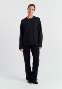 Marineblauer Strickpullover mit geripptem Kragen und Bündchen, kombiniert mit passenden, taillierten Hosen. Sanfte Textur und lockerer Schnitt.