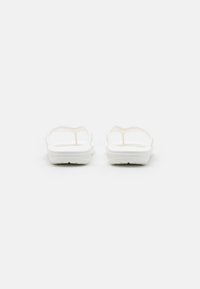 I sandali bianchi presentano un design minimalista con una texture liscia, punta aperta e due ampie cinghie. La suola ha un sottile motivo di battistrada.