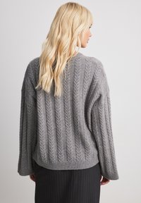 Knitted grey sweater with a textured herringbone pattern, loose fit, wide sleeves, and a ribbed hem, viewed from the back.