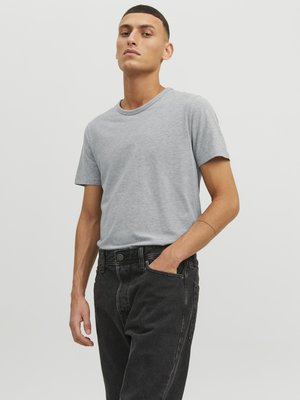 Camiseta gris de manga corta hecha de algodón, combinada con jeans de mezclilla negros de cintura alta. La modelo se encuentra de pie con una mano en el bolsillo, con un fondo neutro.