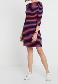 Raidallinen mekko, jossa on tummansinisiä ja punaisia vaakaraitoja, kolmivarrelliset hihat, pyöreä pääntie, valmistettu pehmeästä kankaasta, yhdistetty valkoisiin lenkkareihin.