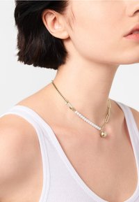 Collier en chaîne dorée avec des accents en perles blanches et un pendentif sphérique, présenté sur un fond uni.