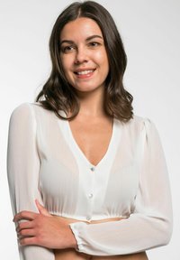 Witte doorzichtige blouse met lange pofmouwen, V-hals en een knoopsluiting. Kenmerkt zich door een gathering aan de onderkant en een textuurstof.