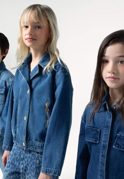 Tre bambini indossano giacche di denim blu, con grandi colli, bottoni dorati e tasche con zip, con varianti nello stile e nella vestibilità dei jeans.
