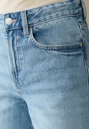 Prim-plan cu o persoană purtând blugi de denim bleu deschis, cu buzunar frontal vizibil, buclă pentru curea și nasture la talie.