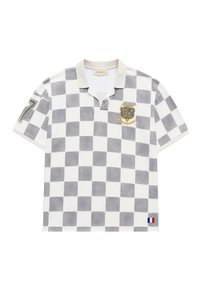 Polo manches courtes avec motif à carreaux gris et blanc, col beige, écusson "Atelier Reternity", numéro 7 sur la manche et petite étiquette drapeau français.
