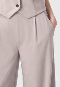 Gilet grigio chiaro su misura con un colletto deciso e due tasche frontali, realizzato in un tessuto liscio e leggermente strutturato.