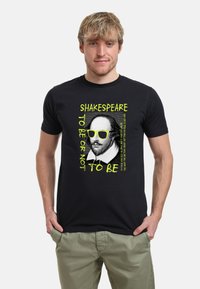 Černé bavlněné tričko s grafikou Shakespeara v žlutých slunečních brýlích a neonově žlutým textem: "SHAKESPEARE BÝT NEBO NEBÝT."