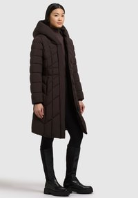 Căciulă pufosă maro cu glugă, cu un model capitonat și mâneci lungi. Așezată lângă bocanci negri până la genunchi și colanți.