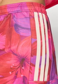 Αθλητικό σορτς με ανθισμένο μοτίβο σε έντονο ροζ και μωβ, με τρεις λευκές κάθετες ρίγες στο πλάι. Κατασκευασμένο από ελαφρύ υλικό.