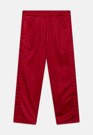 Pantalon de sport rouge avec une taille élastique, poches latérales et une texture lisse et brillante. Présente des coutures verticales sur les côtés.