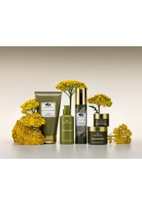 Quatre produits de soin de la peau d'Origins dans un emballage vert et doré, disposés avec des fleurs jaunes. Les tubes et pots texturés présentent des motifs botaniques.