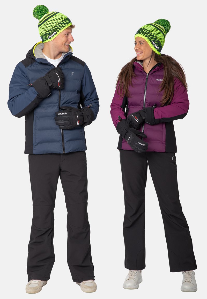 Twee personen in winterkleding. De een draagt een blauwe gewatteerde jas en zwarte broek, de ander een paarse jas en zwarte broek. Beiden dragen bijpassende gebreide mutsen.