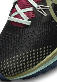 Chaussure de sport noire avec tige en mesh, accents bordeaux contrastants et lacets bleu clair. Présente un talon vert texturé et une semelle extérieure à motifs.