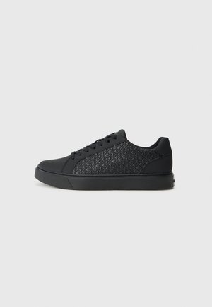 Adidași negri cu un model texturat în formă de diamant pe partea laterală, având vârful rotunjit, talpă plată și închidere cu șireturi.