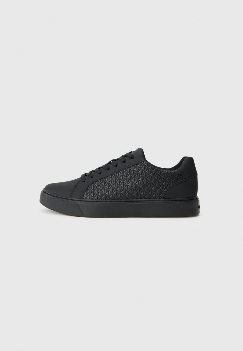 Adidași negri cu un model texturat în formă de diamant pe partea laterală, având vârful rotunjit, talpă plată și închidere cu șireturi.