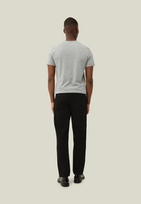 T-shirt cinza de manga curta, vista por trás, combinada com calças pretas e sapatos pretos. Design simples, ajuste casual, sem padrões visíveis.
