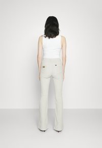 Ljust grå utsvängda jeans med hög midja och två bakfickor. Materialet har en slät textur och har en liten märkeslogotyp nära midjebandet.