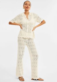Lace-stickad TVÅ-delad outfit i elfenben med en kragad kortärmad skjorta och vida byxor, med ett zickzackmönster och vågiga kanter.