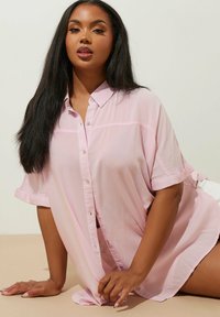 Ljusrosa knapplistad skjorta i genomskinligt tyg, med krage, uppvikta ärmar och avslappnad passform som hänger lätt över kroppen.