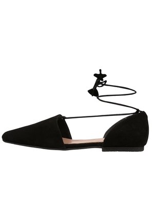 Zapato plano de ante negro con punta puntiaguda, laterales abiertos y lazos para atar alrededor del tobillo con un lazo en la parte trasera.