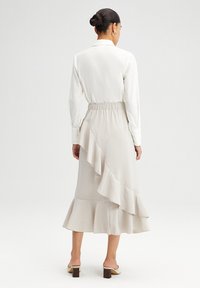 Blusa ligera color crema con cintura ajustada, combinada con una falda larga y fluida de color beige que presenta un dobladillo con volantes en capas.