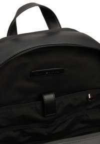 Zaino nero con esterno in pelle liscia. L'interno presenta un rivestimento in tessuto morbido, chiusura a zip e scomparti per l'organizzazione.