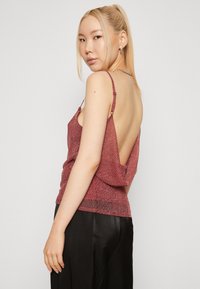 Rode glitterachtige backless top met dunne bandjes en een gedrapeerd ontwerp, met een gestructureerde afwerking. Gecombineerd met zwarte satin broeken.