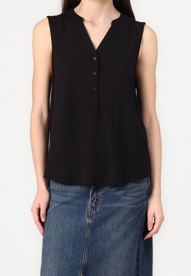 Top nero senza maniche con un discreto scollo a V, dettagli con bottoni e una vestibilità rilassata, realizzato in un materiale liscio. Abbinato a una gonna di jeans.
