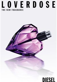 Herzförmige Parfümflasche aus lila Glas mit facettiertem Design, silbernem Sprühkopf und dezentem Branding an der Seite. Reflektierende Oberfläche.