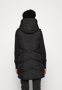 Gilet rembourré noir avec capuche, doté de coutures en chevrons et de manches texturées, fabriqué en tissu lisse et léger.