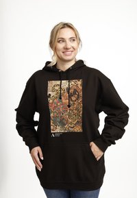 Sudadera negra con un colorido estampado gráfico de tigres y figuras. Diseñada con un bolsillo frontal y capucha ajustable con cordón.