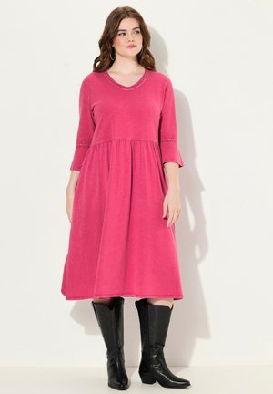 Abito rosa al ginocchio con scollatura rotonda e maniche a tre quarti, con vita arricciata e cuciture decorative. Indossato con stivali neri.