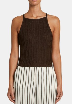 Donna che indossa un top senza maniche, marrone scuro, in maglia a coste abbinato a pantaloni bianchi a vita alta con strisce verticali marroni.