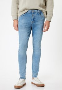 Jeans in denim azzurro chiaro con vestibilità slim, caratterizzati da un classico design a cinque tasche e una leggera scoloritura. Abbinati a sneaker bianche e beige.