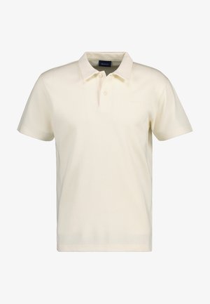 Polo à manches courtes couleur crème avec col et patte de boutonnage à deux boutons, présentant un tissu légèrement texturé et un petit logo de la marque sur la poitrine.