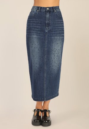 Gonna midi in denim con vita alta, lavaggio blu scuro, decorazioni con borchie e silhouette dritta. Abbinata a scarpe con zeppa nere.