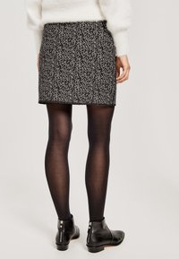 Spódnica w czarno-białe plamki o dopasowanym kształcie, w połączeniu z czarnymi, nieprzezroczystymi rajstopami oraz botkami za kostkę z zamkiem błyskawicznym.