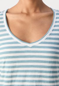 Gros plan sur la partie supérieure de la poitrine et le cou d'une personne portant une chemise à encolure en V rayée bleue et blanche.